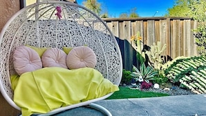 A hanging chair with cushions and a yellow blanket, a wooden fence, and various cacti and plants in the background. - Garden vibes - 3BR Home near Downtown (San Jose)