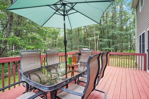A glass-top table with four chairs and a green umbrella on a wooden deck.