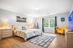 A bedroom with a bed, bedside lamps, a window, a chair, and a TV.