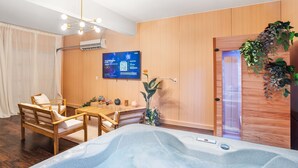 Una habitación moderna con suelo de madera, una silla de madera, una peque ña mesa, un televisor montado en la pared y una puerta decorada con una planta colgante.