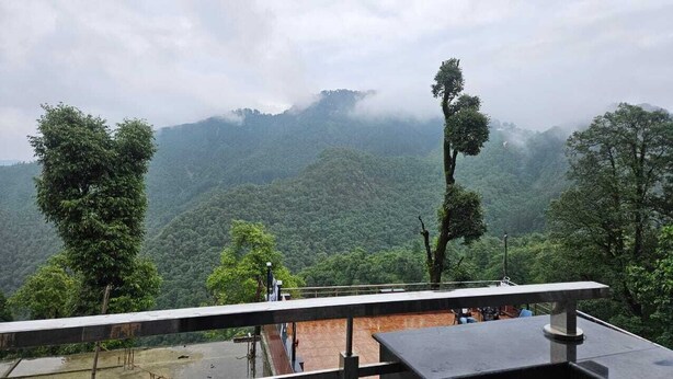 Vista desde un balcón sobre un paisaje montañoso exuberante con vegetación densa y picos cubiertos de niebla.