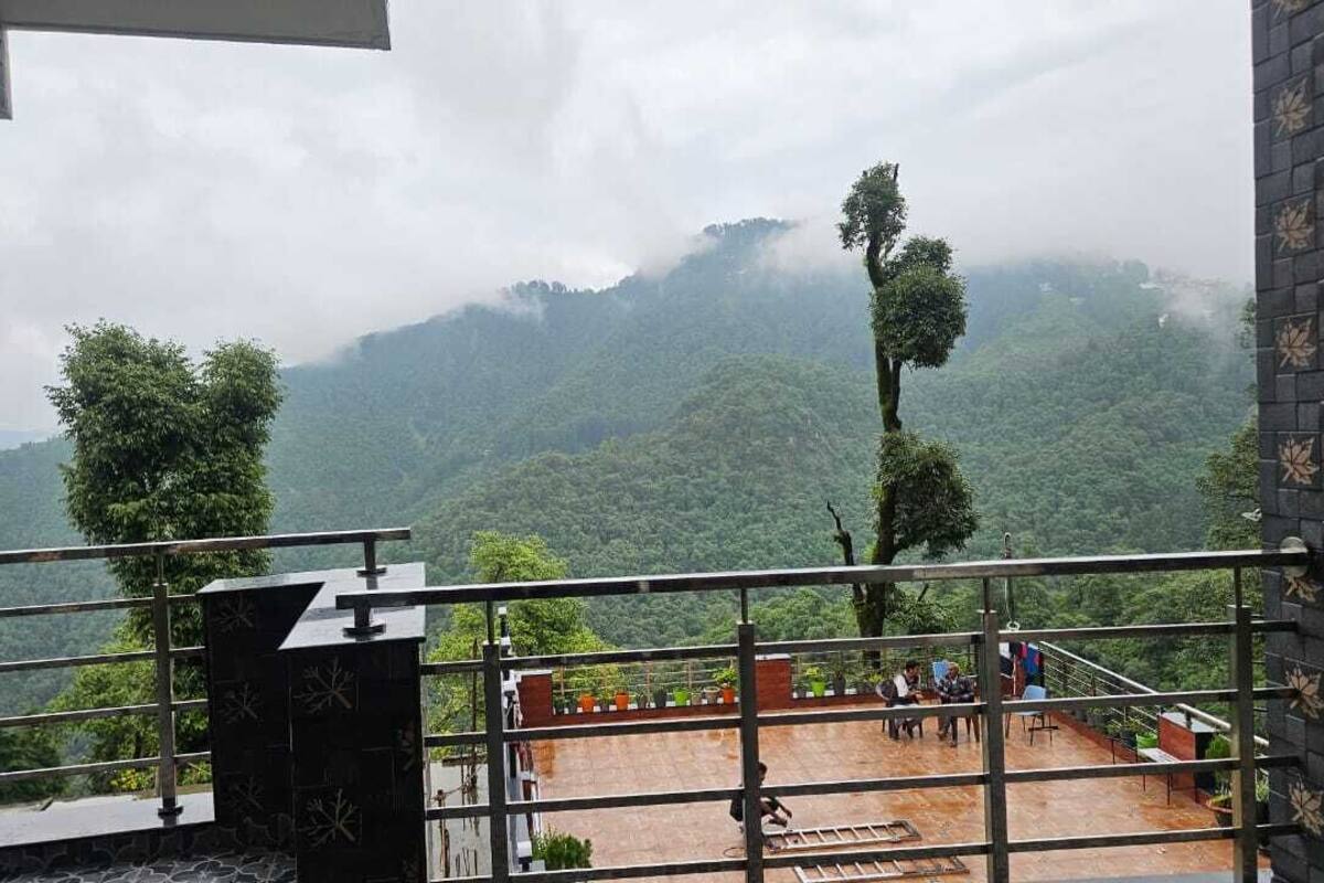 Una terraza con vistas a montañas verdes y exuberantes, una barandilla y algunas personas.