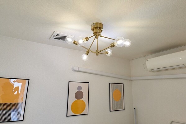 A ceiling with a brass chandelier and air conditioning vents. There are three framed artworks on the wall.