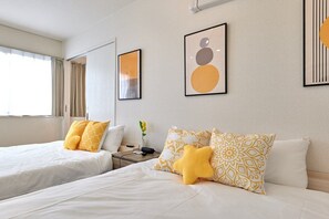 A hotel room with two beds, a nightstand, a vase with flowers, and abstract wall art.