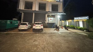 Un edificio di due piani con un cartello che riporta “Hotel Paramhans”. Due auto sono parcheggiate davanti, una motocicletta e un generatore verde sulla sinistra.