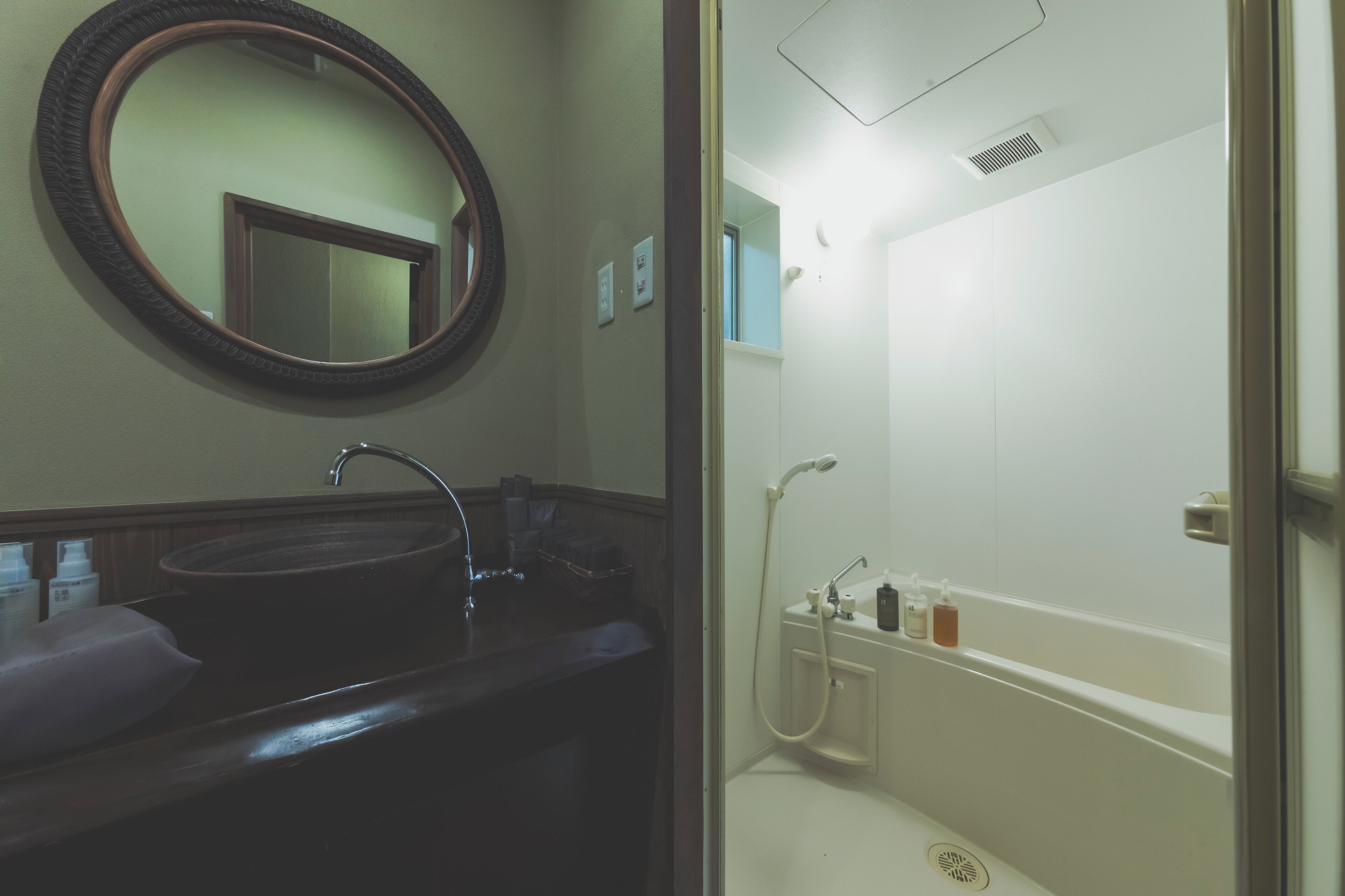 Une salle de bain avec un miroir rond, un lavabo et une baignoire équipée d’un pommeau de douche.