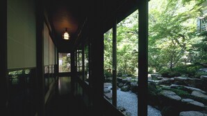 Un couloir doté d’un plancher en bois et de grandes fenêtres, qui mène à un jardin agrémenté de rochers et de verdure.