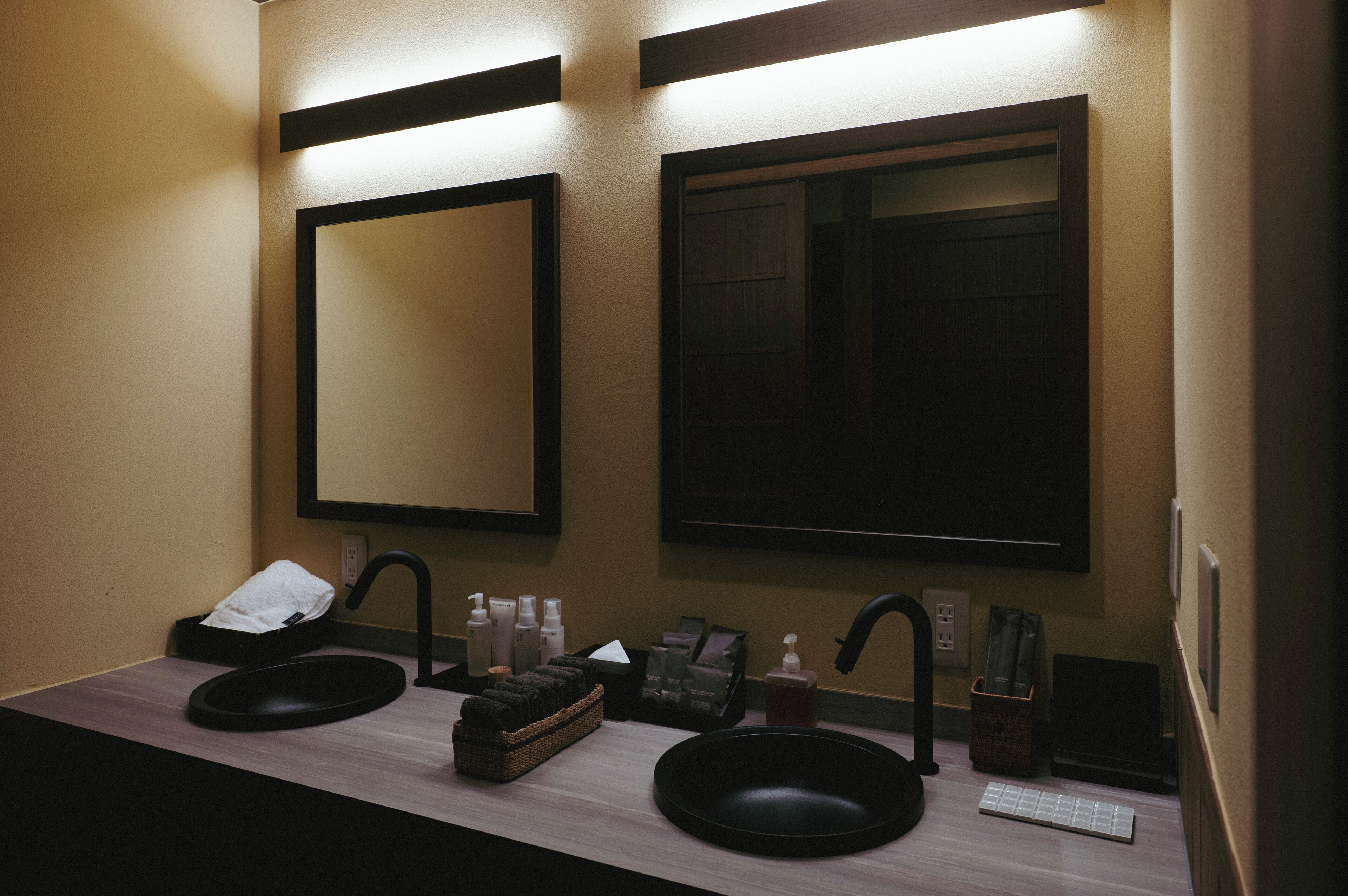 A bathroom with two sinks, a mirror, and a shelf with toiletries.