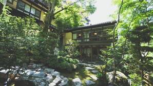 Un bâtiment de style japonais traditionnel, entouré d’une végétation luxuriante et de sentiers pavés de pierres.