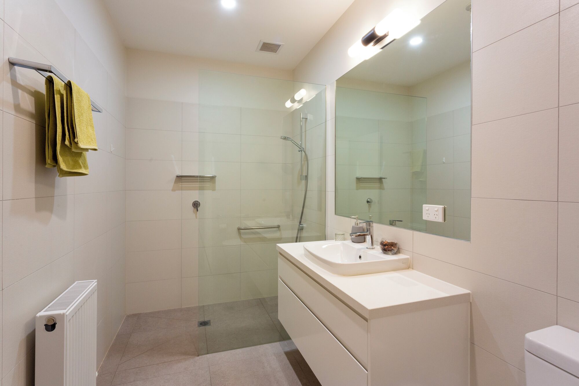 A modern bathroom with a glass shower enclosure, a white sink, and a large mirror.