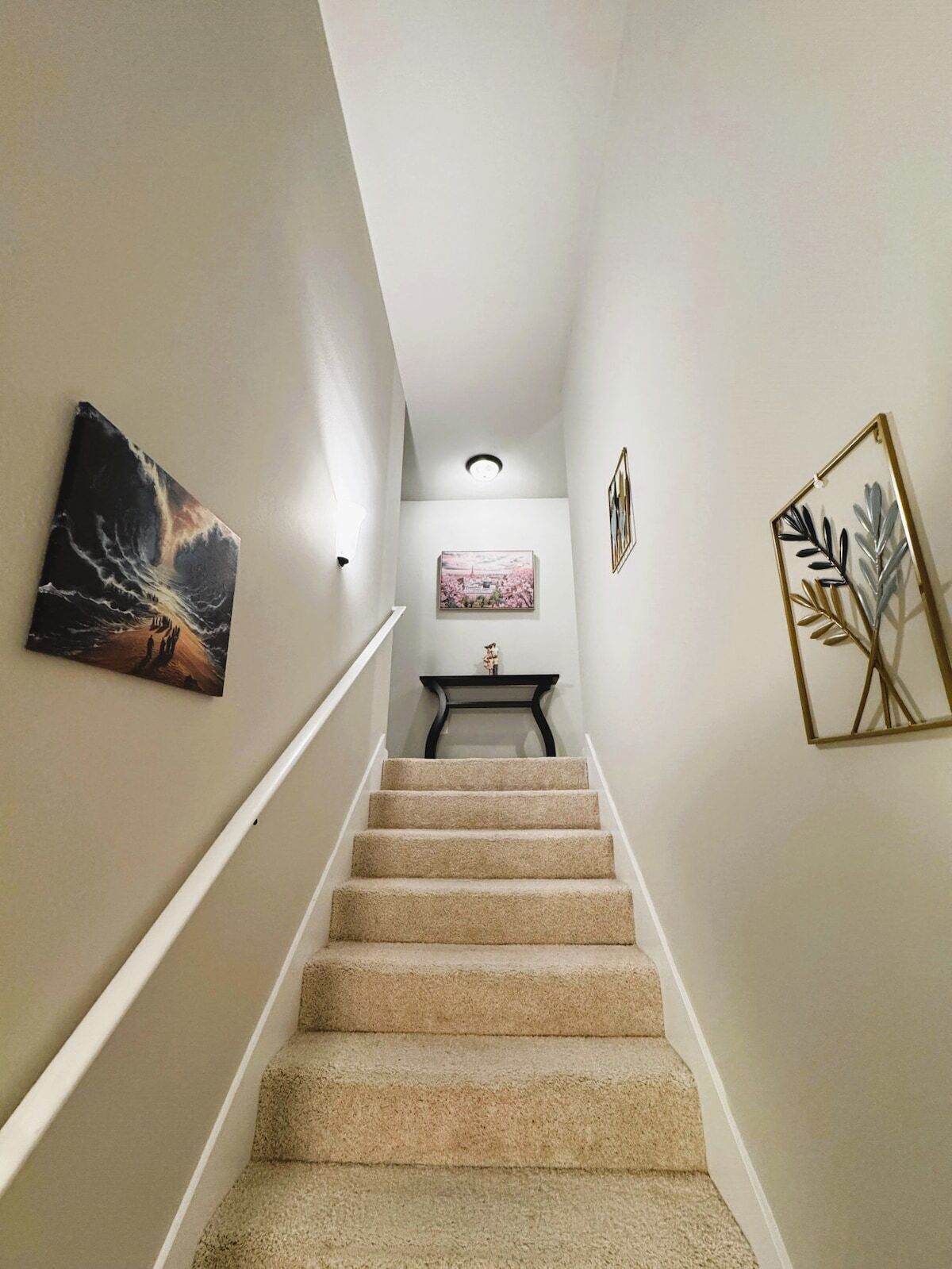 A carpeted staircase with a handrail, leading to a landing with a small table and a framed picture.