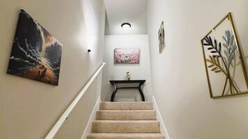 A carpeted staircase with a handrail, leading to a landing with a small table and a framed picture.
