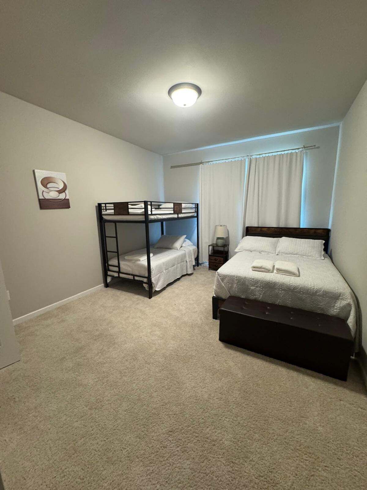 A bedroom with bunk beds, a single bed, a bedside table, and a lamp.