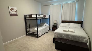 A bedroom with bunk beds, a single bed, a bedside table, and a lamp.