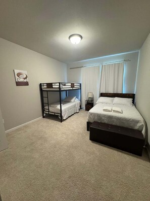 Une chambre avec des lits superposés, un lit simple, une table de chevet et une lampe.