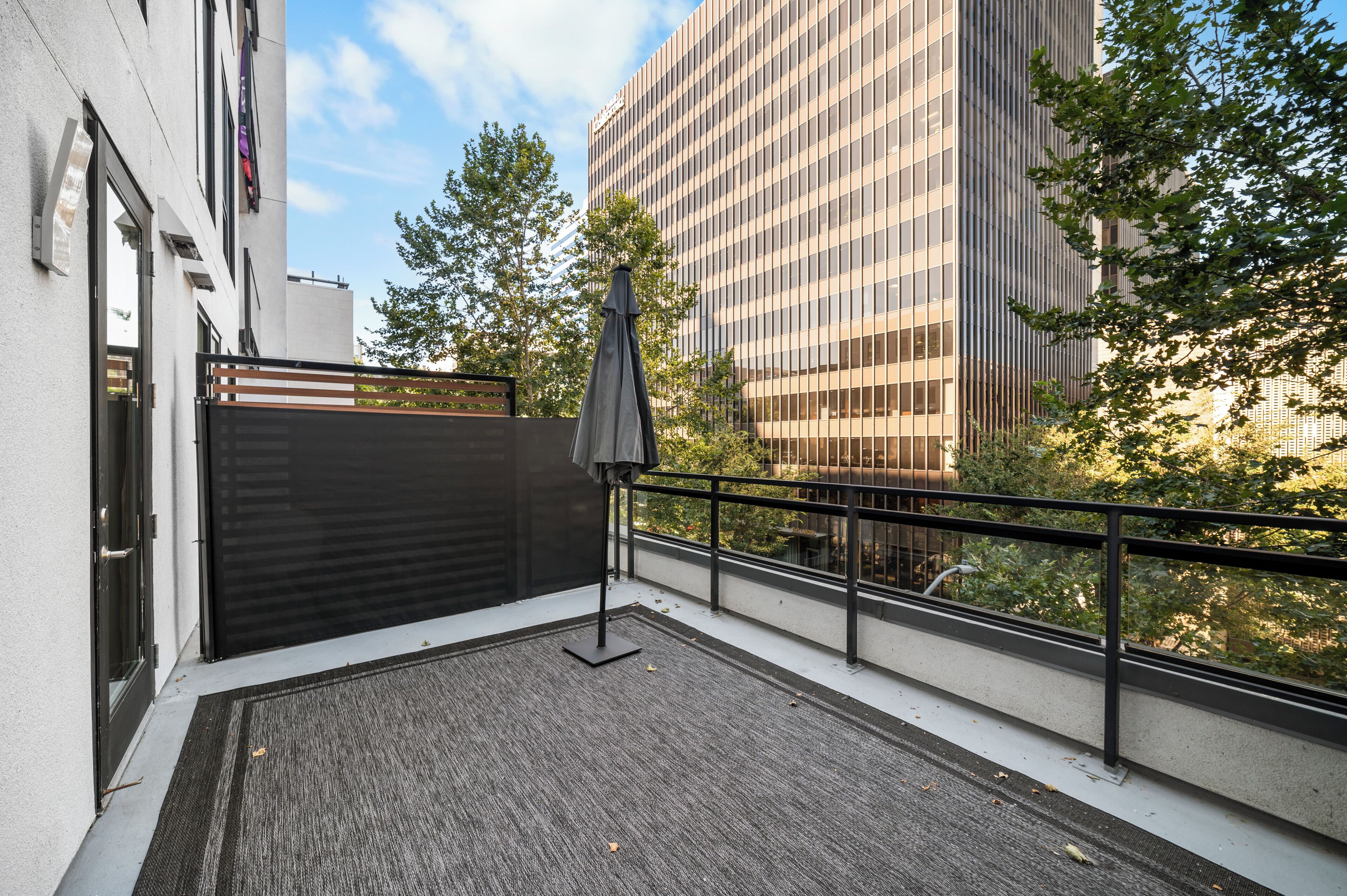 A balcony with a black metal railing, a grey carpet, and a grey umbrella.