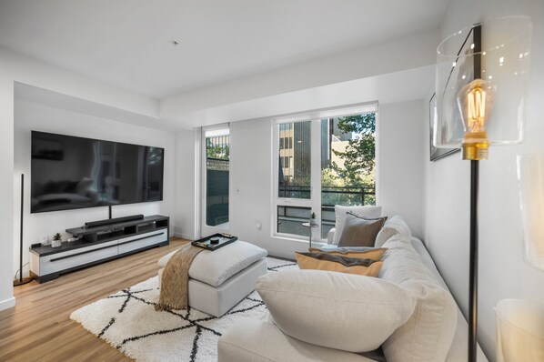 A modern living room with a large flat-screen TV, a white sofa, a coffee table, and a floor lamp.