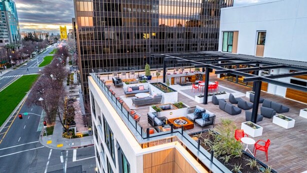 Eine Dachterrasse mit Außenbestuhlung und Blick auf die Stadt, im Hintergrund ein modernes Gebäude.