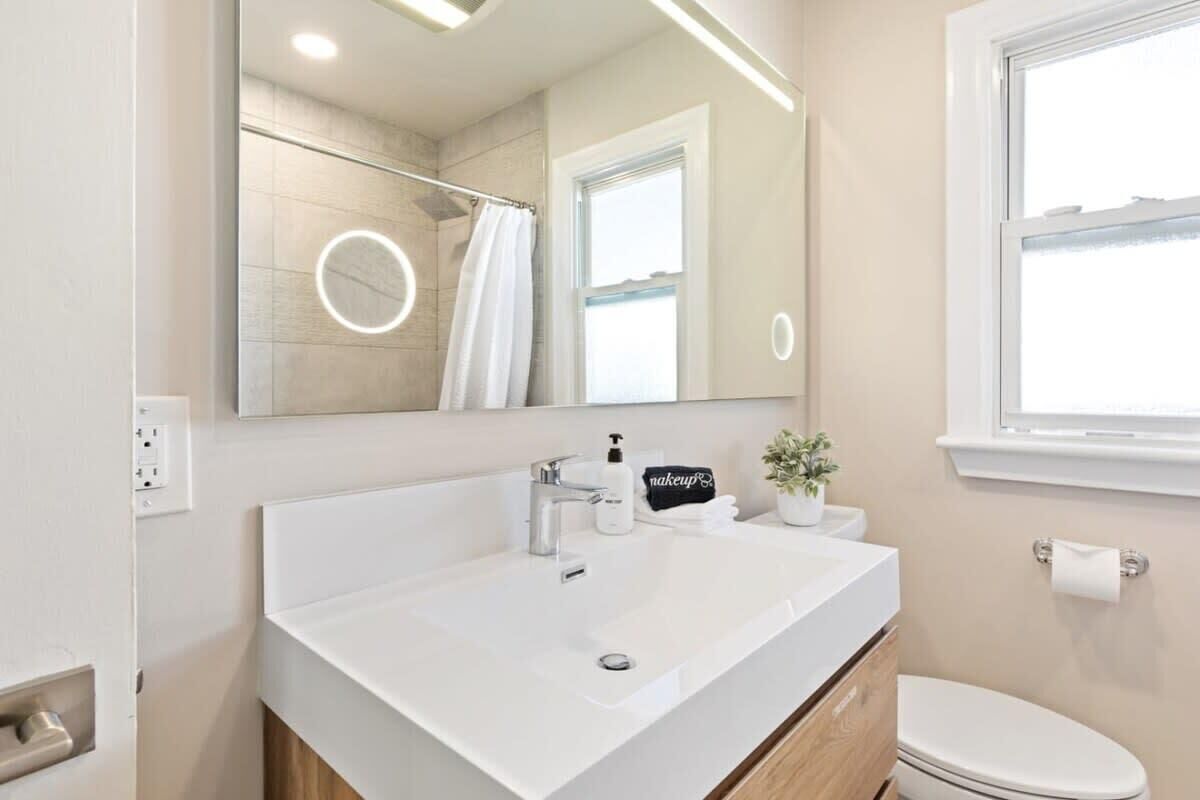 A modern bathroom with a white sink, a mirror, a shower curtain, and a toilet.