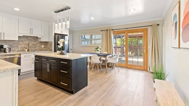 A modern kitchen with a central island, white cabinets, and a dining area with a table and chairs. - @ Marbella Lane - Modern Refreshing Home (San Mateo)