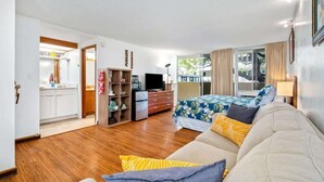 A spacious bedroom with a large bed, a sofa, and a TV. There is a kitchen area visible through an open door. - @ Marbella Lane -coastal Retreat Near Diamond Head (Honolulu)