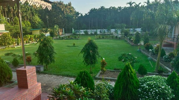 A lush garden with a well-maintained lawn, various shrubs, and a brick structure. - SUMARU JUNGLE RESORT (Alipurduar)
