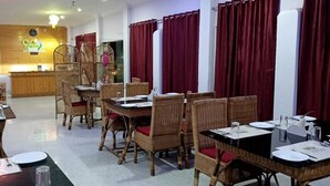 A restaurant with wicker furniture, red curtains, and a reception area with a wooden counter. - SUMARU JUNGLE RESORT (Alipurduar)