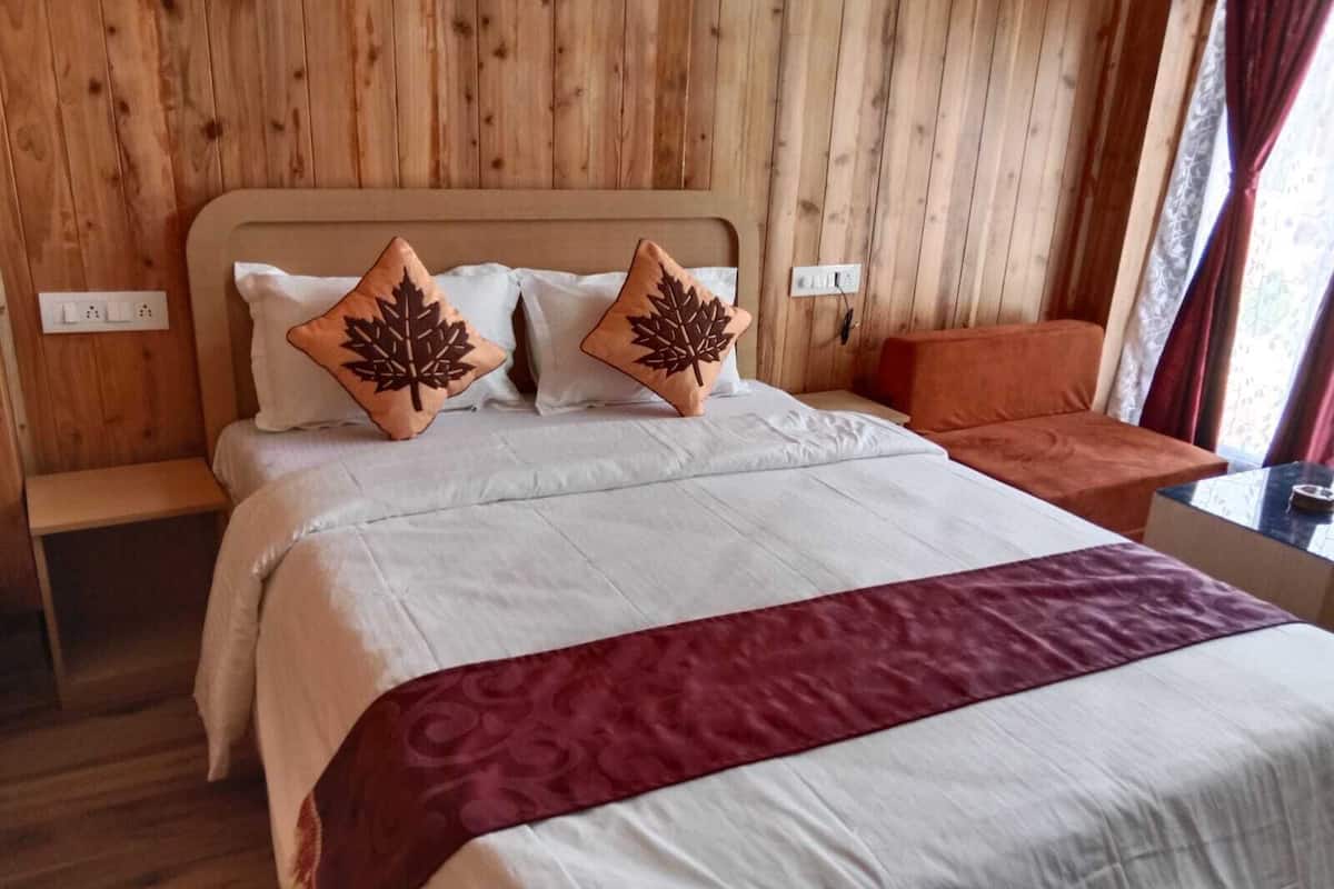 Uma cama bem arrumada com edredom branco e vinho, duas almofadas com padrão de folha e cabeceira de madeira.