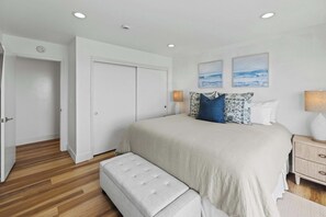 A bedroom with a bed, a bench, a nightstand, a lamp, and two wall-mounted pictures.