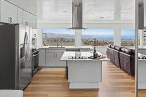A modern kitchen with a central island, stainless steel appliances, and a view of the city. - New 3B 3BA Panoramic Ocean Views 30 Night Min (Seaside)