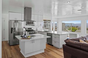 A modern kitchen with a central island, stainless steel appliances, and a view of the outdoors. - New 3B 3BA Panoramic Ocean Views 30 Night Min (Seaside)