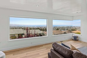 A spacious room with large windows offering a city view, a brown leather sofa, and a wooden floor.