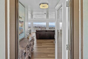 A modern interior with a wooden dining table, a dark leather sofa, and large windows offering a city view. - New 3B 3BA Panoramic Ocean Views 30 Night Min (Seaside)