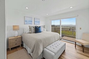 A bedroom with a large bed, a nightstand, a bench, and a balcony with a view.
