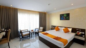 A hotel room with a large bed, a desk, two chairs, a small table, and a painting on the wall. - Renai Sreekrishna (Guruvayur)