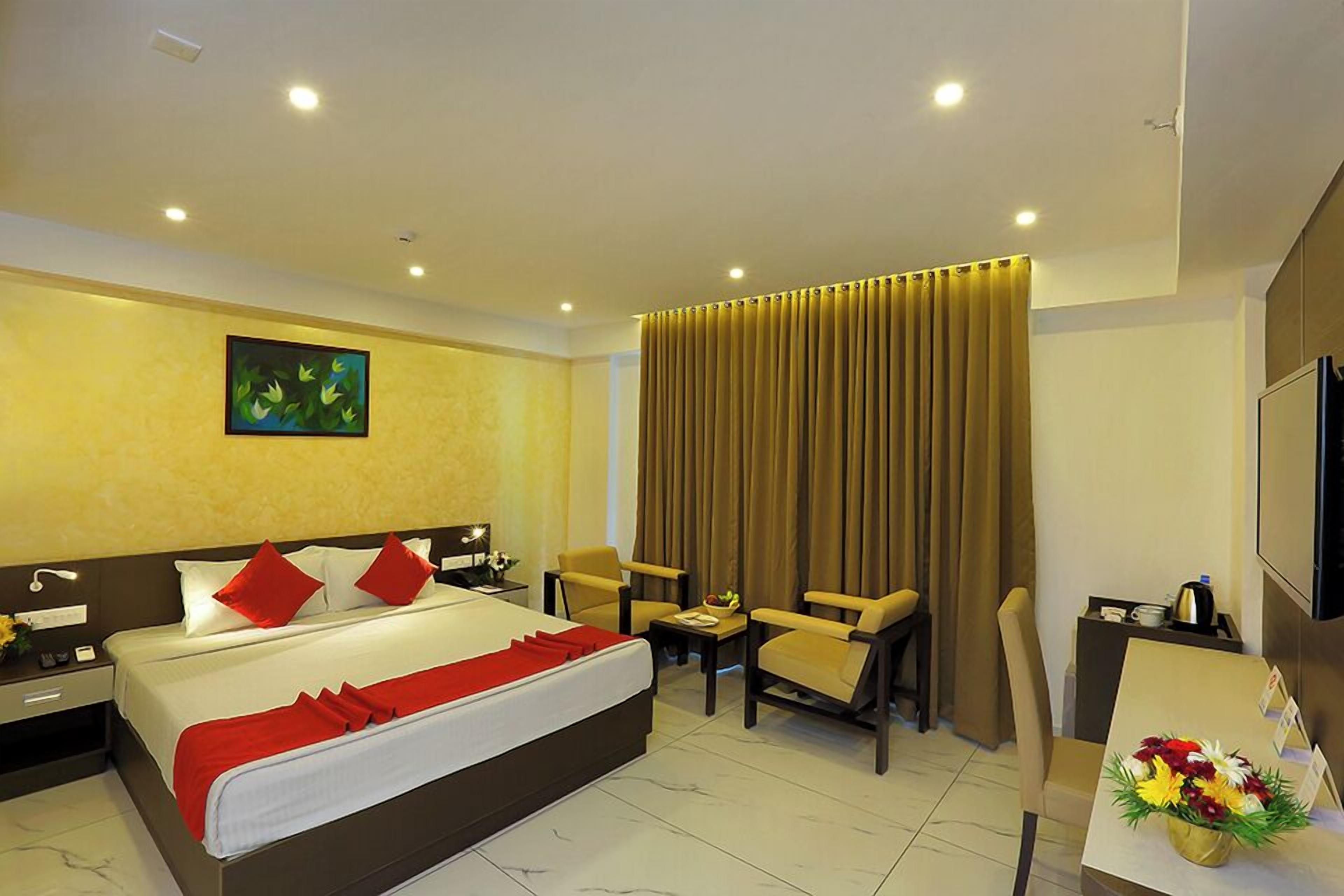 A hotel room with a large bed, two armchairs, a desk with a TV, and a painting on the wall.