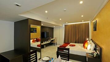 Quarto de hotel com cama, escrivaninha, cadeira, televisão e área de jantar com mesa posta para dois.