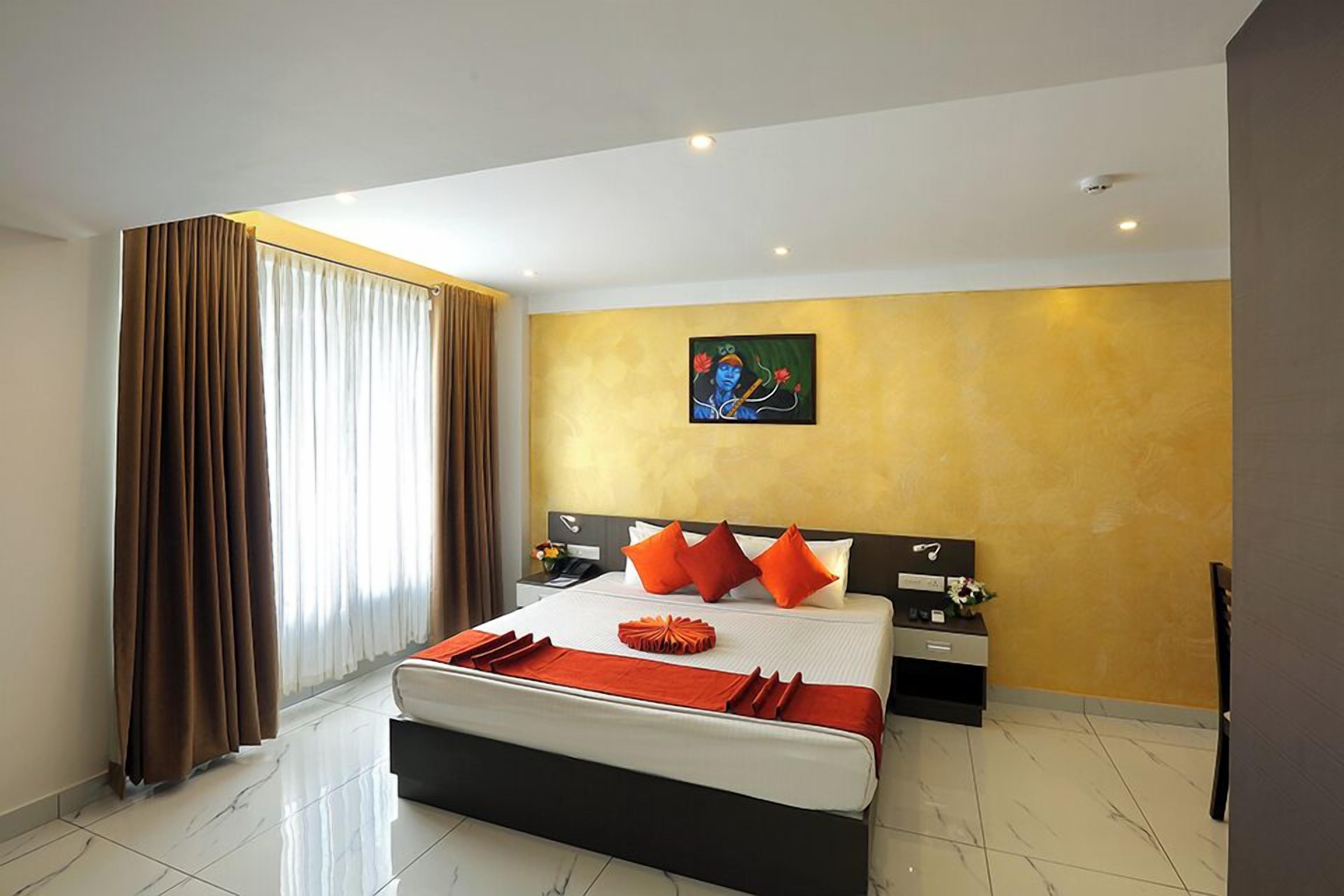 A hotel room with a large bed, a nightstand, a painting on the wall, and a window with curtains.
