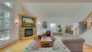 A spacious living room with a fireplace, large windows, and a staircase. - Creek Dips & S’mores: Catskills Gem (Phillipsport)