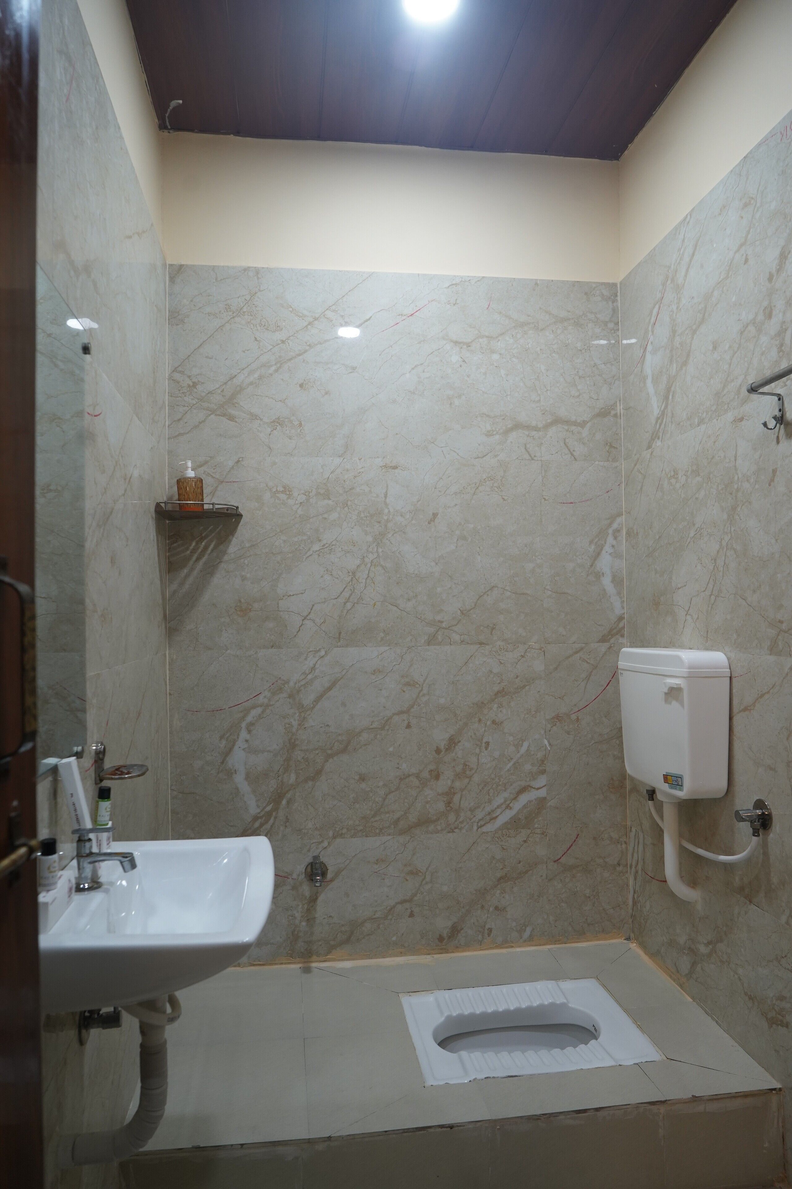 A bathroom with a marble wall, a sink, a toilet, and a soap dispenser.