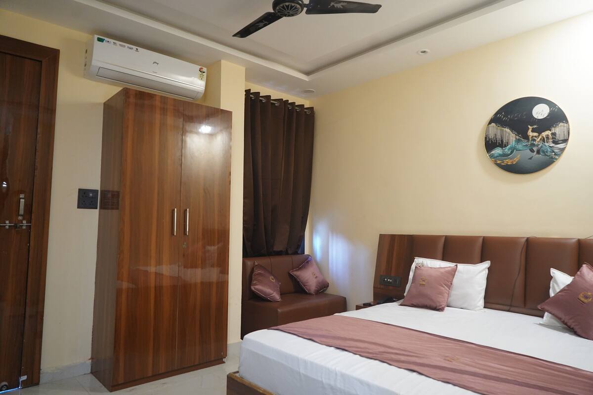 Quarto de hotel com cama, guarda-roupa, ventoinha no teto e aparelho de ar condicionado, além de uma obra de arte pendurada na parede.