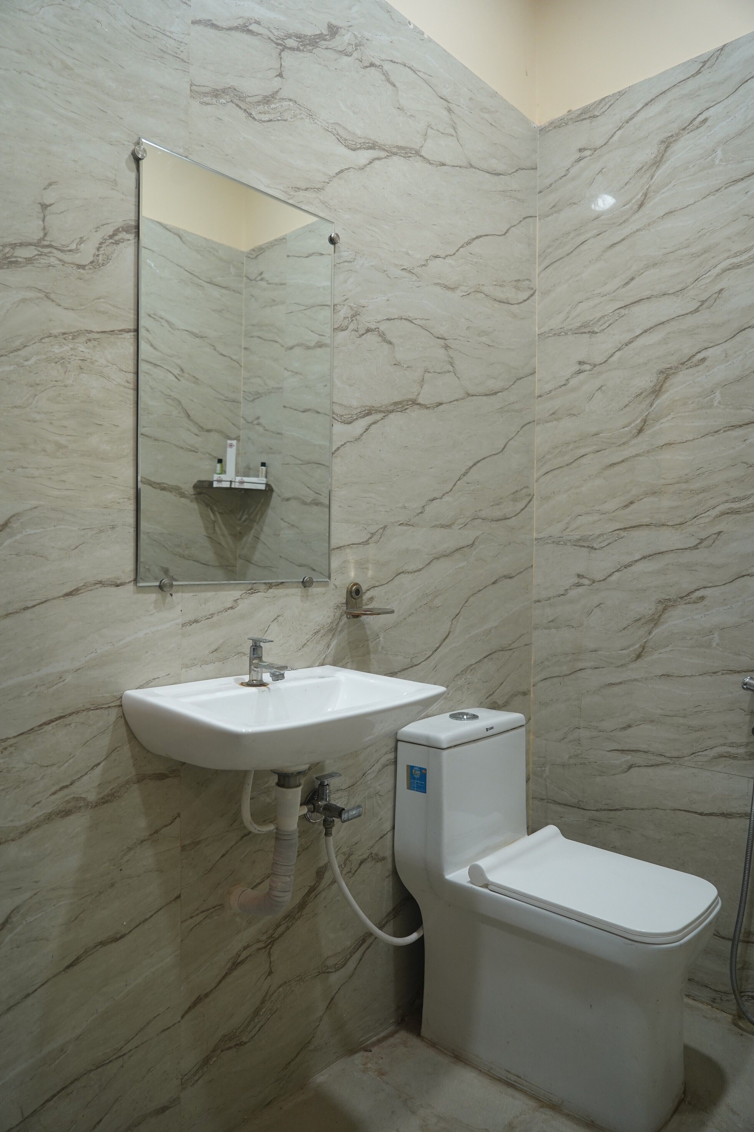 A bathroom with a marble wall, a sink, a toilet, and a mirror.