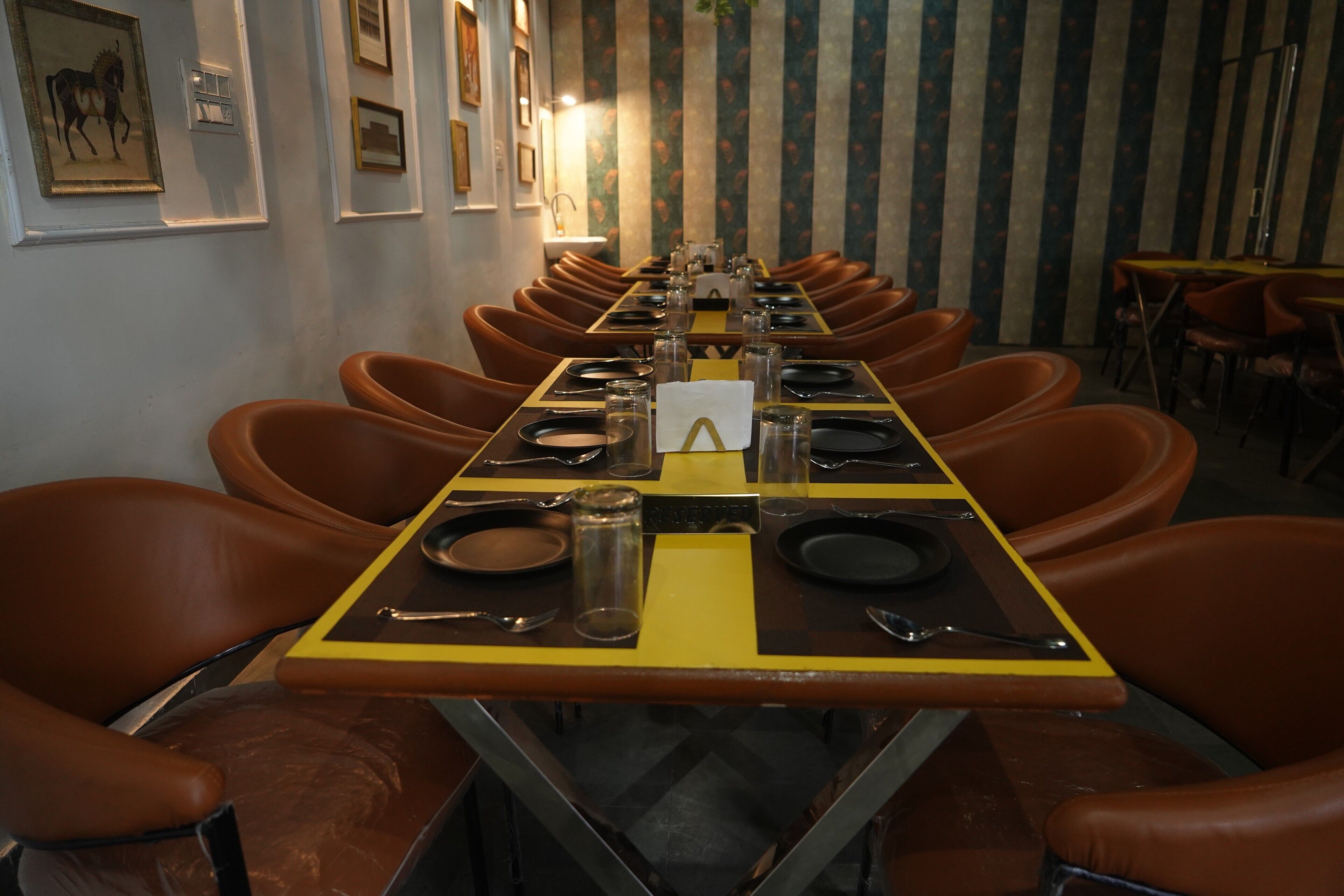 Una larga mesa de comedor dispuesta con sillas, cuadros enmarcados en la pared y un fondo de papel tapiz a rayas.