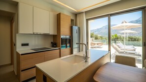 A modern kitchen with a built-in oven and a large window overlooking a patio with outdoor furniture. - Villa Zen Chrysi – Vacation villa in Crete (Georgioupolis)