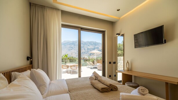 A hotel room with a large bed, a flat-screen TV, and a balcony with a mountain view. - Villa Zen Chrysi – Vacation villa in Crete (Georgioupolis)