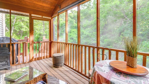 Una terraza de madera con una mesa de vidrio, una parrilla y vistas a un bosque.