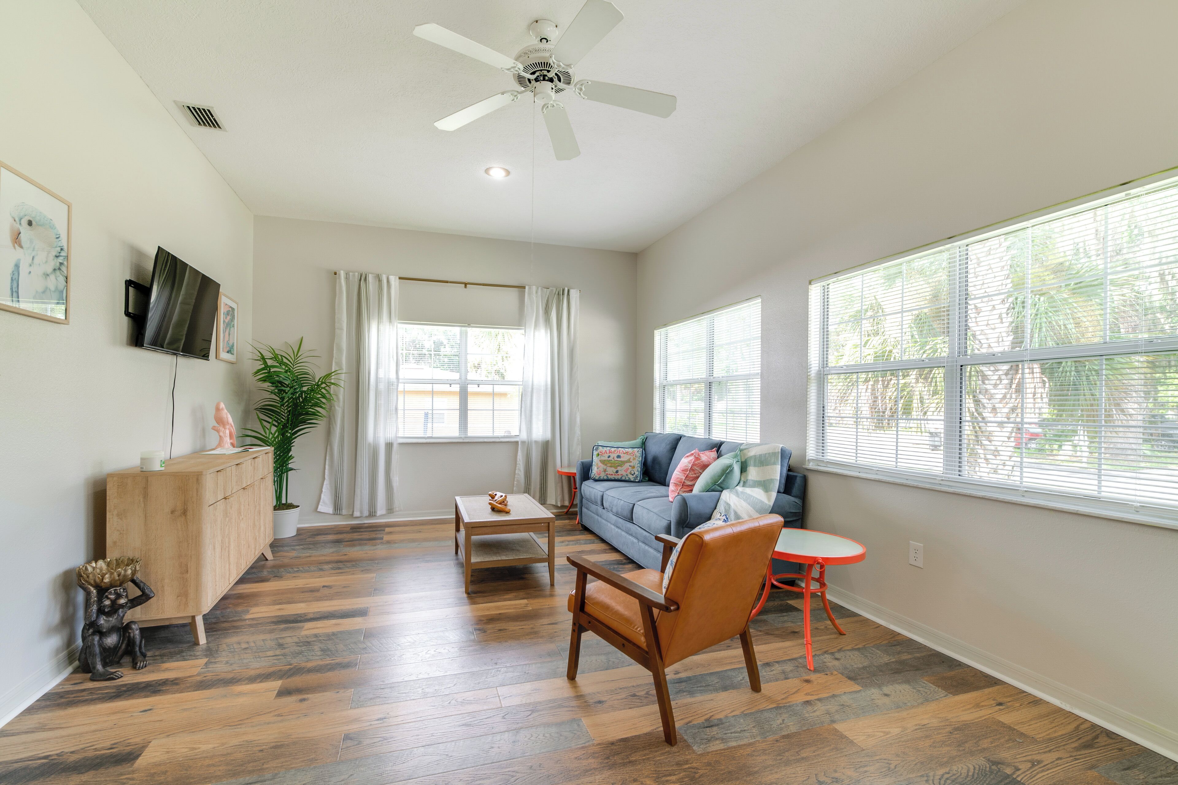 Un salon spacieux doté d  ’un parquet, d’un ventilateur de plafond, d’un canapé, d’une table basse et d’une petite table orange.