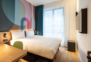 A hotel room with a bed, a desk, a chair, a TV, and a window with curtains. - B&B HOTEL Brussels Airport (Machelen)