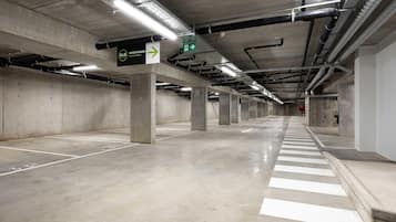 Un amplio estacionamiento subterráneo con pilares de hormigón, señalización direccional y un ambiente limpio y bien iluminado.