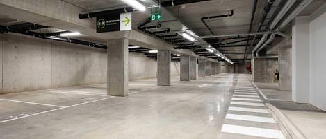 Un amplio estacionamiento subterráneo con pilares de hormigón, señalización direccional y un ambiente limpio y bien iluminado.